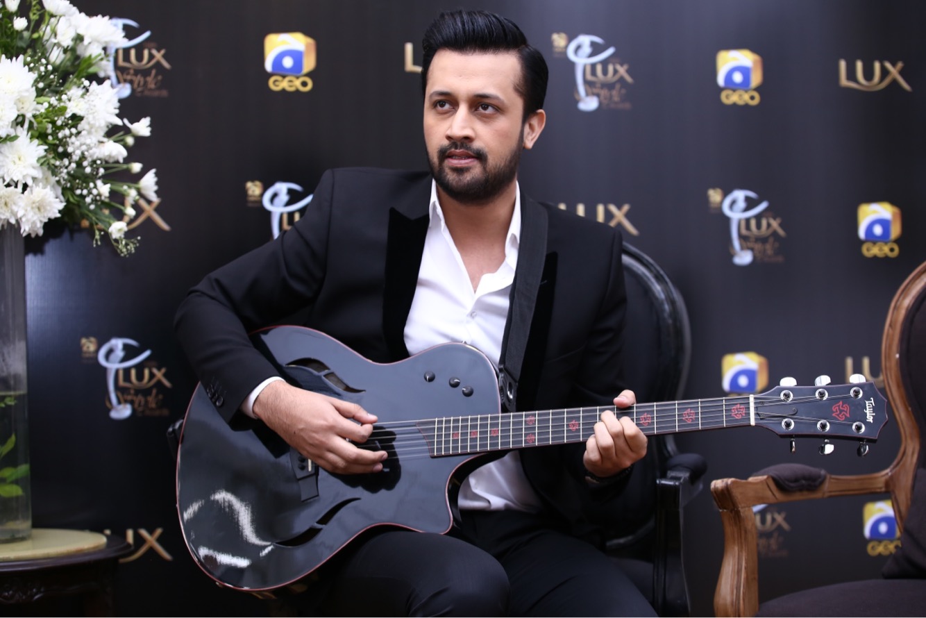 Atif Aslam with guitar in black suit.